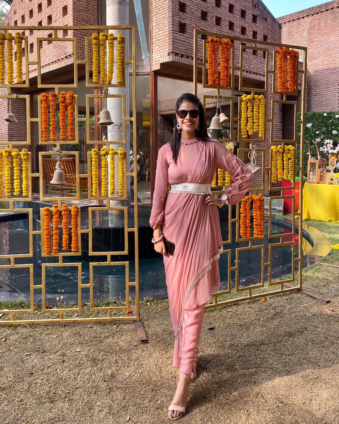 Model is wearing a fusion saree gown in blush pink draped georgette saree-style top and cotton silk cigarette pants with embellished belt – occasion wear by Prisella